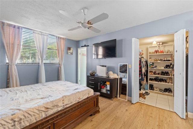 bedroom featuring a walk in closet, ceiling fan, a closet, and light wood-type flooring