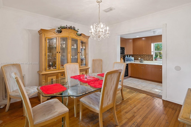 dining room with light wood-type flooring, ornamental molding, and a notable chandelier