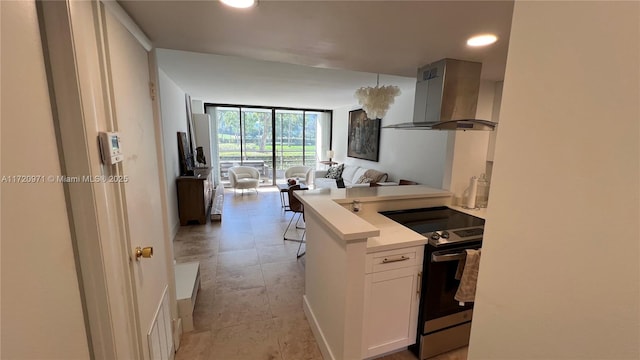 kitchen with a wall of windows, stainless steel range with electric stovetop, white cabinetry, wall chimney exhaust hood, and open floor plan