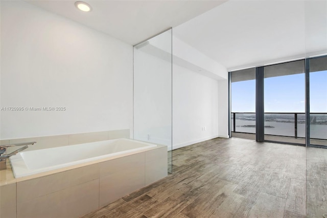 bathroom with hardwood / wood-style floors, expansive windows, and tiled bath