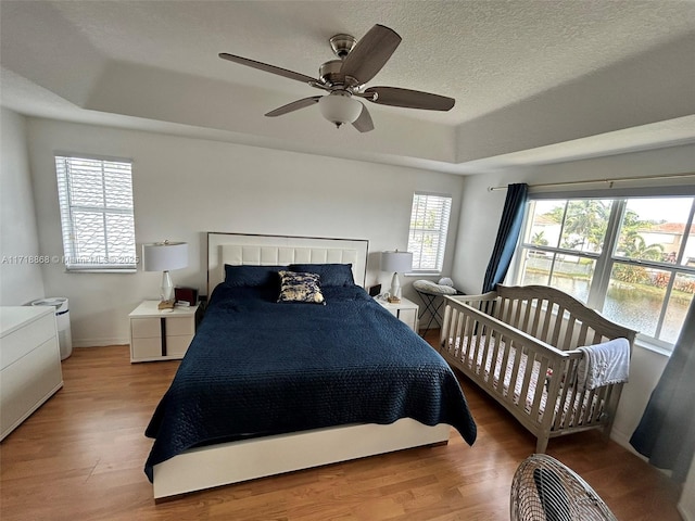 bedroom featuring a tray ceiling, ceiling fan, hardwood / wood-style floors, and a textured ceiling