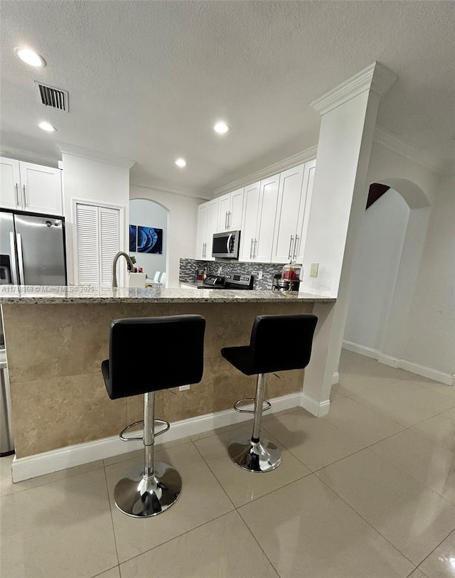 kitchen featuring white cabinets, a kitchen breakfast bar, light stone counters, kitchen peninsula, and stainless steel appliances