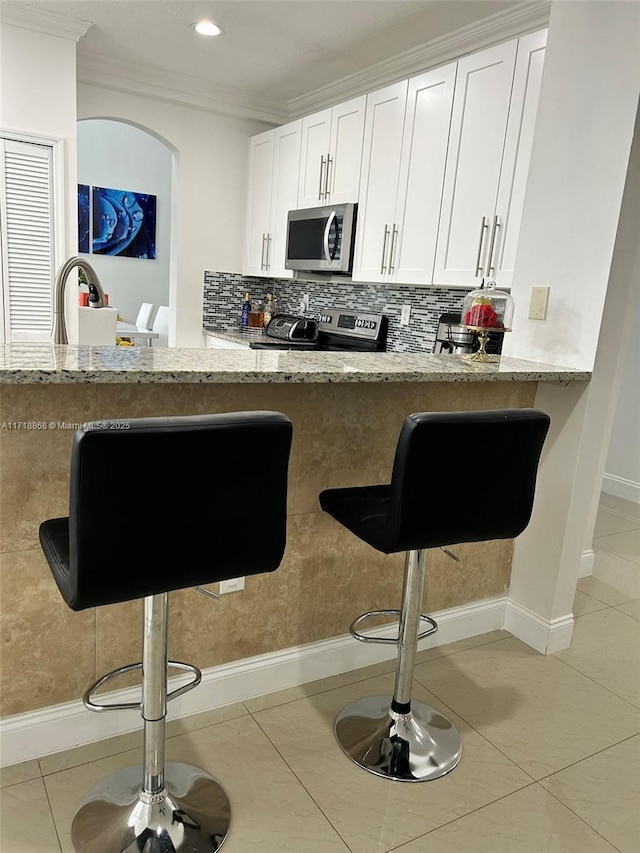 kitchen featuring white cabinets, appliances with stainless steel finishes, light stone counters, and a breakfast bar area