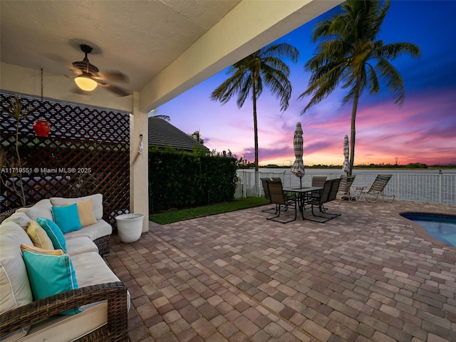 patio terrace at dusk featuring a fenced in pool, ceiling fan, and an outdoor living space