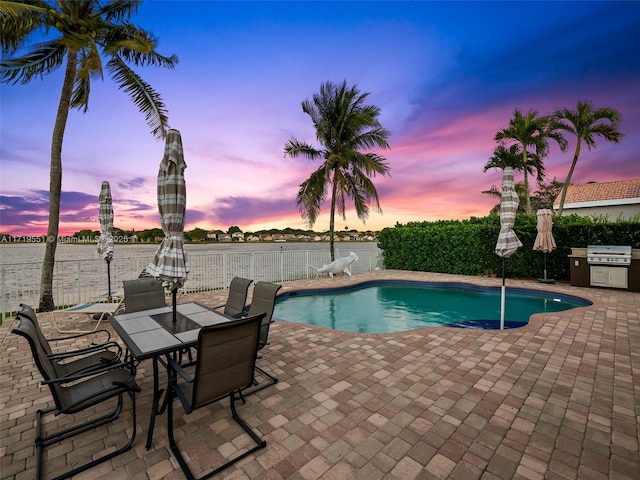 pool at dusk with a water view, grilling area, and a patio area