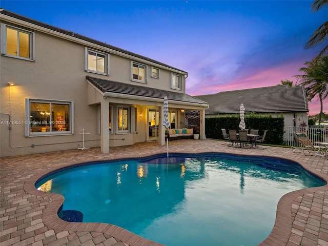 pool at dusk with outdoor lounge area and a patio area