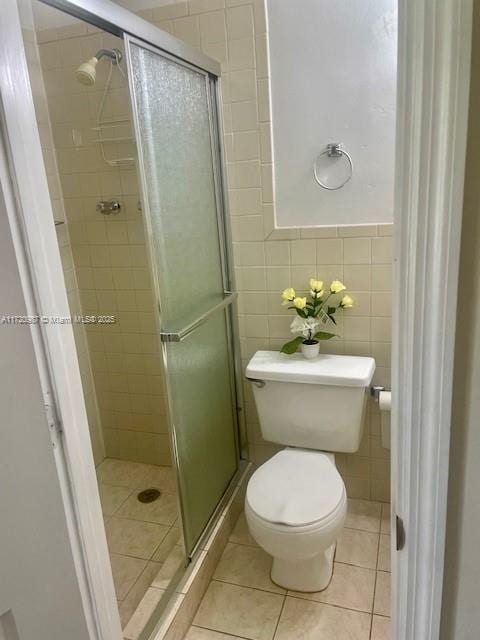 bathroom with tile patterned flooring, toilet, an enclosed shower, and tile walls