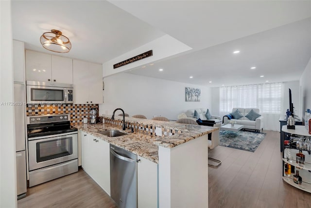 kitchen featuring kitchen peninsula, appliances with stainless steel finishes, light stone counters, sink, and white cabinetry