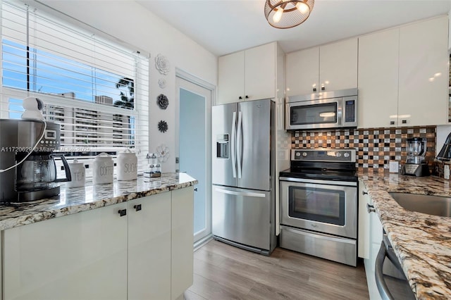 kitchen with white cabinetry, tasteful backsplash, light stone counters, light hardwood / wood-style floors, and appliances with stainless steel finishes