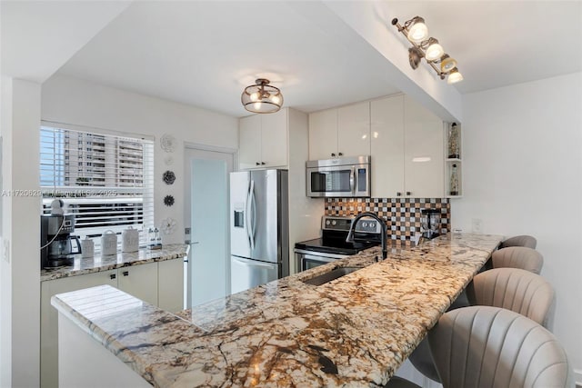 kitchen featuring white cabinetry, sink, stainless steel appliances, kitchen peninsula, and a kitchen bar