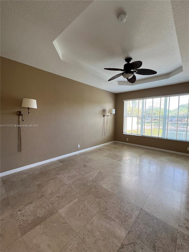 empty room featuring a textured ceiling, a raised ceiling, and ceiling fan