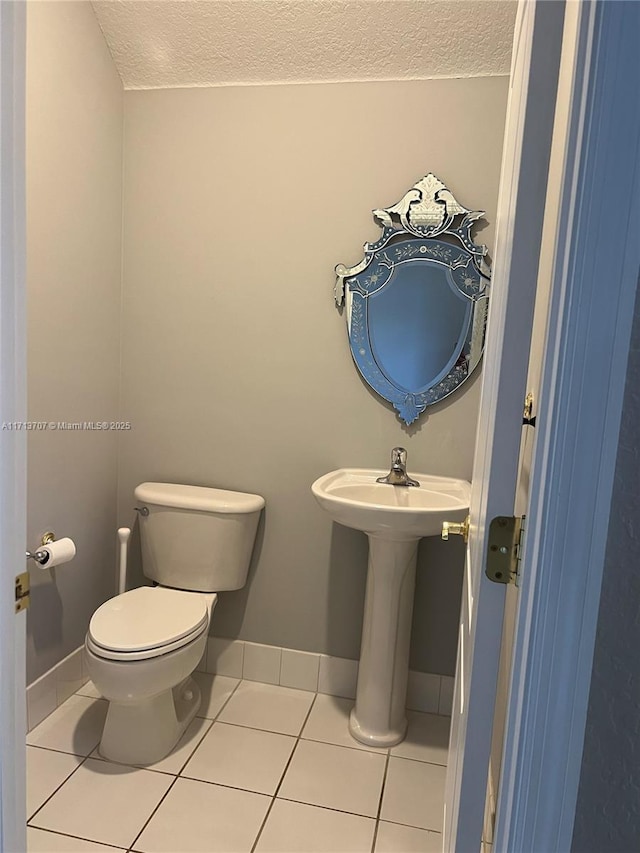 bathroom with tile patterned flooring, a textured ceiling, toilet, and sink