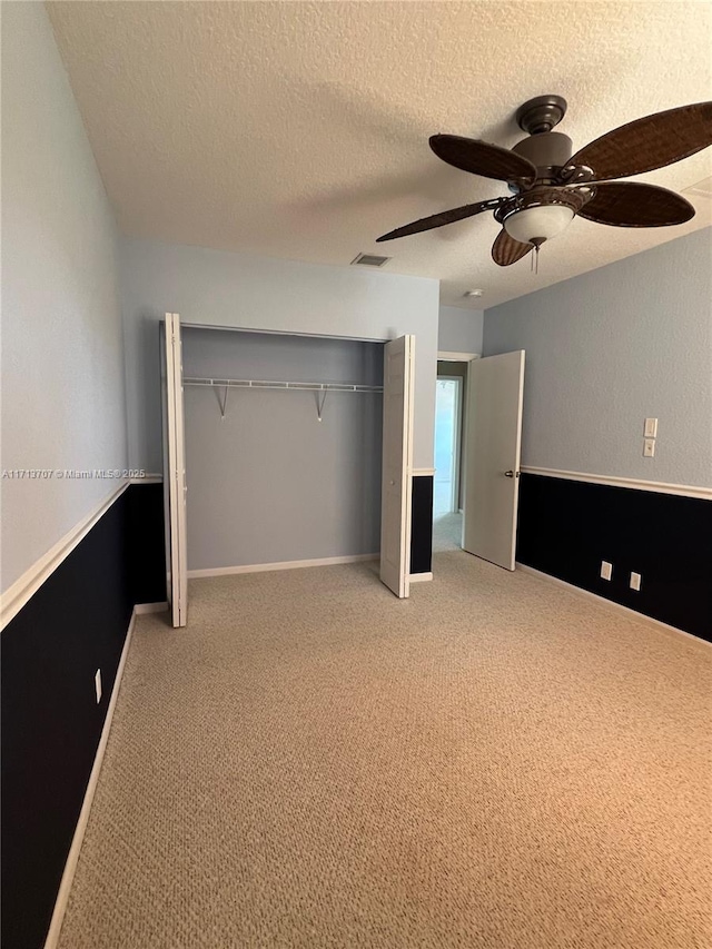 unfurnished bedroom featuring light carpet, a textured ceiling, a closet, and ceiling fan