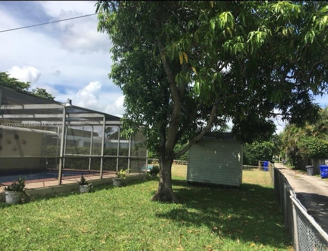 view of yard with an outdoor structure, fence, glass enclosure, a storage unit, and an outdoor pool