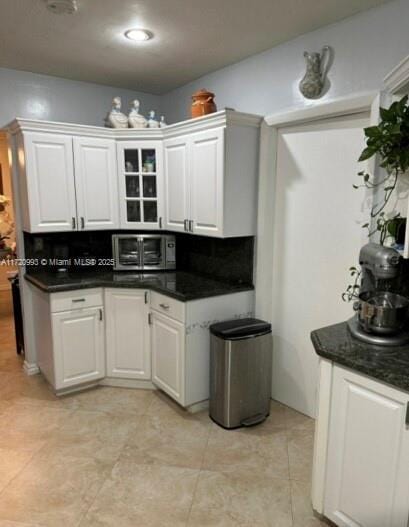 kitchen with a toaster, dark countertops, white cabinetry, and glass insert cabinets