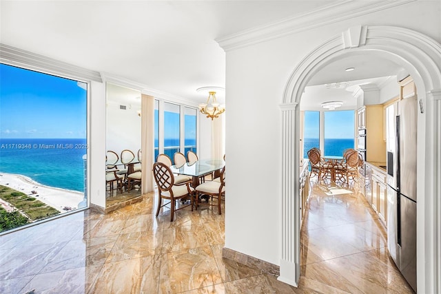 dining area with a healthy amount of sunlight, crown molding, a chandelier, a view of the beach, and a water view