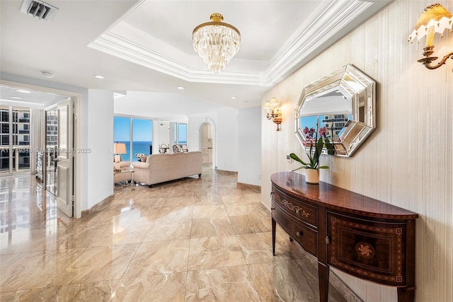 hall featuring a tray ceiling, an inviting chandelier, crown molding, and a water view