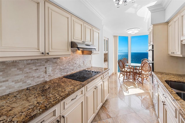 kitchen with backsplash, dark stone countertops, cream cabinetry, black electric stovetop, and a water view