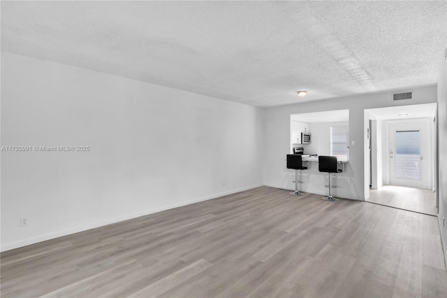 unfurnished living room with light wood-type flooring and a textured ceiling