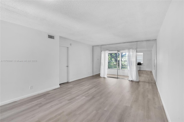 empty room with light wood-type flooring and a textured ceiling