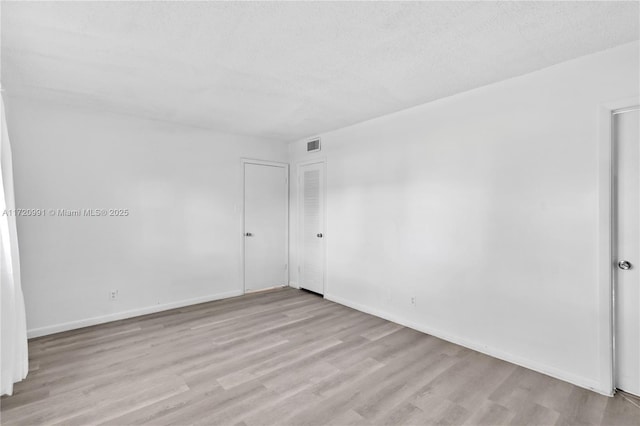 unfurnished room with light wood-type flooring and a textured ceiling