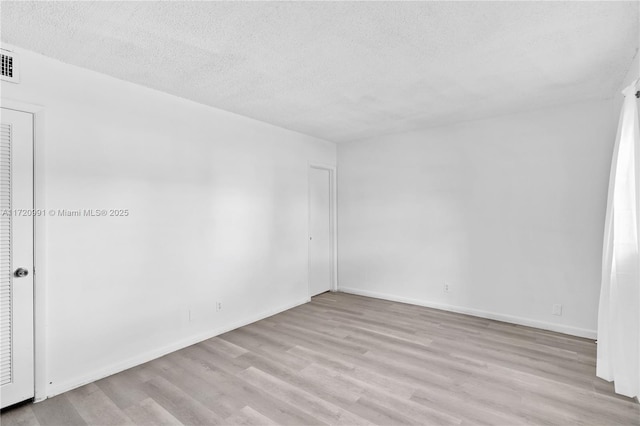 empty room with light wood-type flooring and a textured ceiling