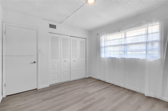 unfurnished bedroom with light hardwood / wood-style flooring, a textured ceiling, and a closet