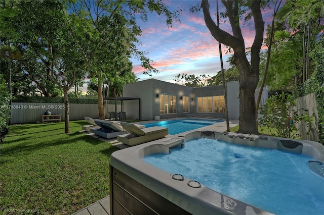 pool at dusk with a yard and a hot tub