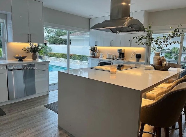 kitchen with hardwood / wood-style floors, white cabinets, stainless steel dishwasher, island range hood, and a breakfast bar area