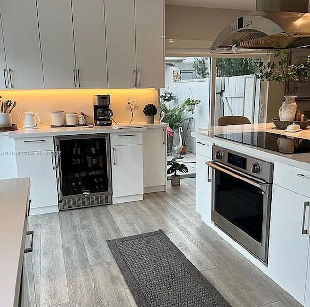 kitchen with white cabinetry, oven, beverage cooler, and exhaust hood