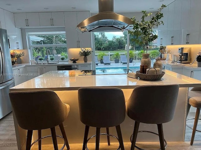 kitchen featuring stainless steel fridge, island range hood, a center island, white cabinetry, and a breakfast bar area