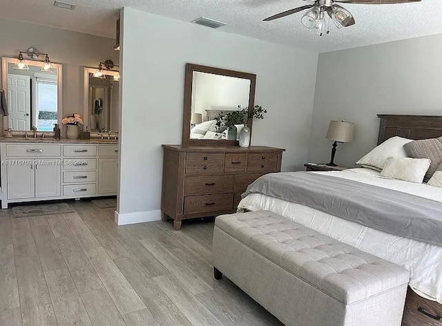 bedroom featuring ceiling fan, sink, light wood-type flooring, and a textured ceiling