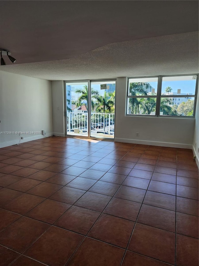 unfurnished room with a textured ceiling, plenty of natural light, and dark tile patterned flooring