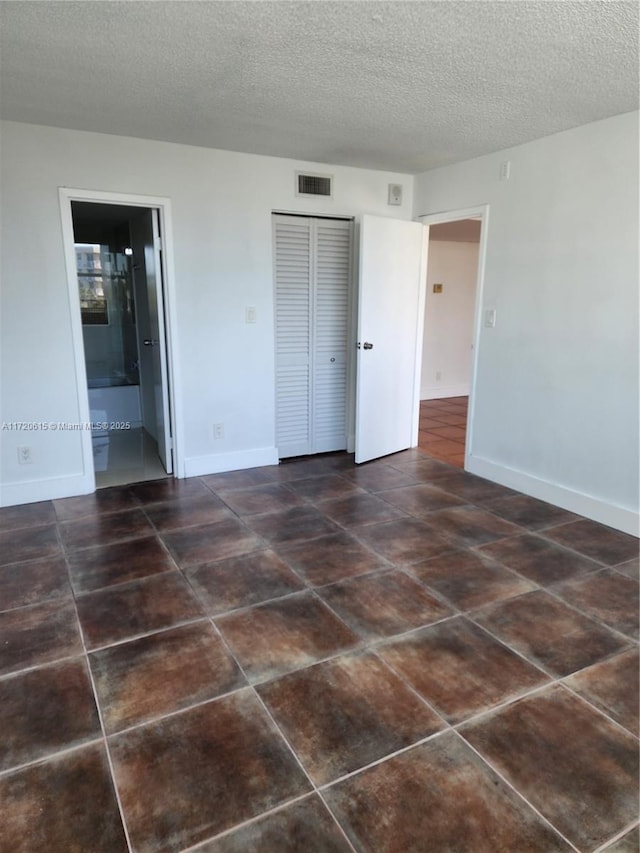 unfurnished bedroom with a textured ceiling, ensuite bathroom, and a closet