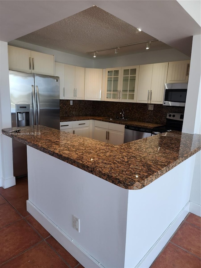 kitchen with kitchen peninsula, appliances with stainless steel finishes, rail lighting, and dark tile patterned flooring