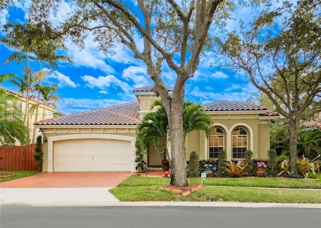 mediterranean / spanish-style house featuring a garage, fence, driveway, a tiled roof, and stucco siding