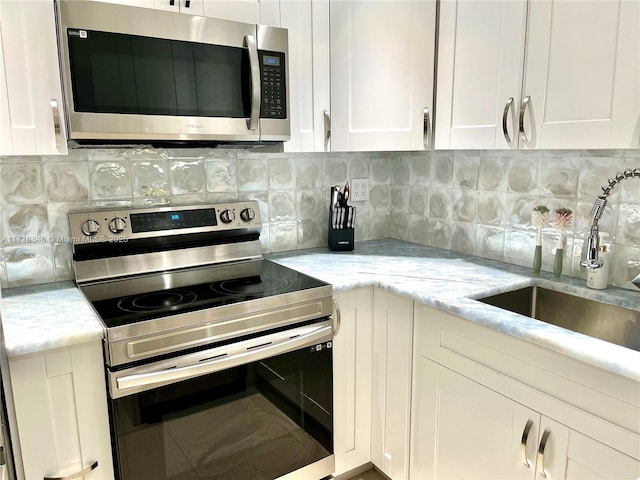 kitchen with sink, decorative backsplash, light stone counters, white cabinetry, and stainless steel appliances