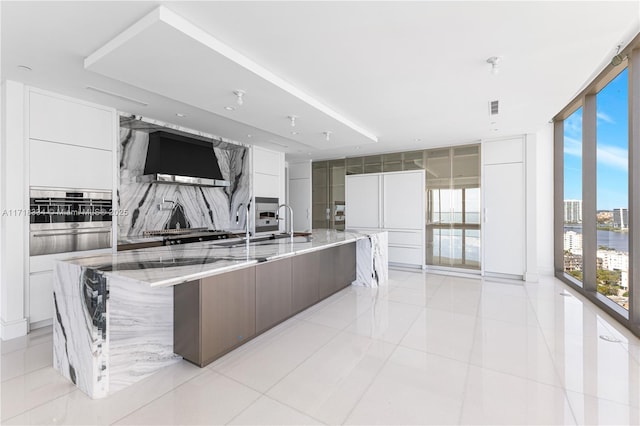 kitchen featuring white cabinets, a wall of windows, a spacious island, and wall chimney exhaust hood