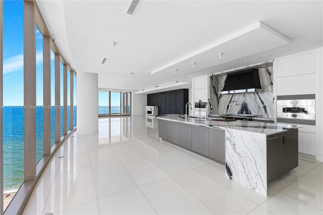 kitchen with white cabinets, a water view, a large island, and wall chimney range hood