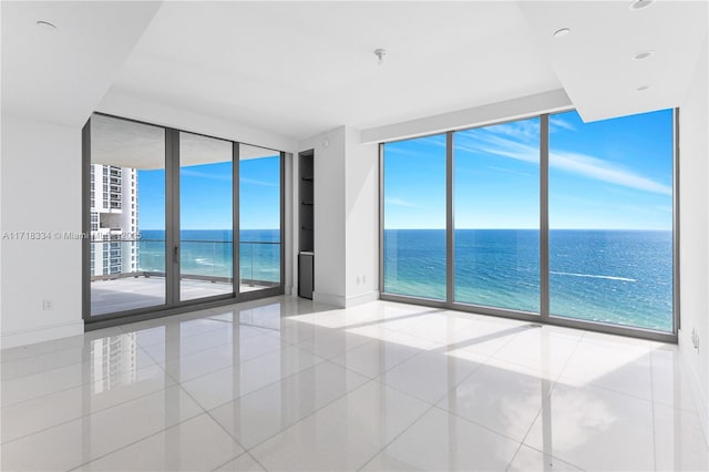 spare room featuring light tile patterned floors, a water view, a wall of windows, and built in shelves