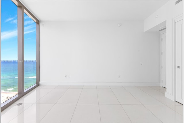 tiled empty room with a beach view, a water view, a wall of windows, and a healthy amount of sunlight