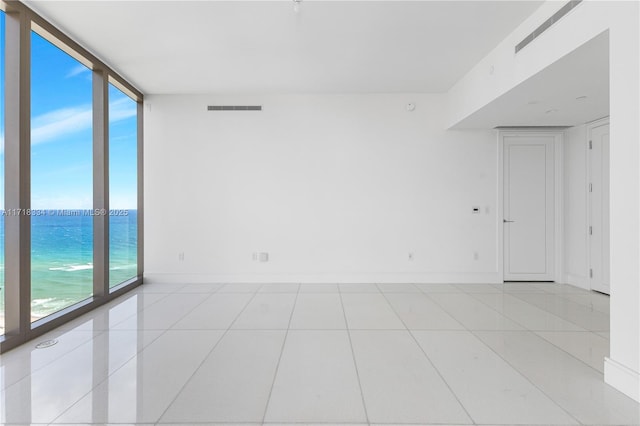 empty room featuring a water view, light tile patterned floors, and a wall of windows