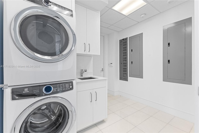 laundry room featuring electric panel, cabinets, sink, and stacked washing maching and dryer