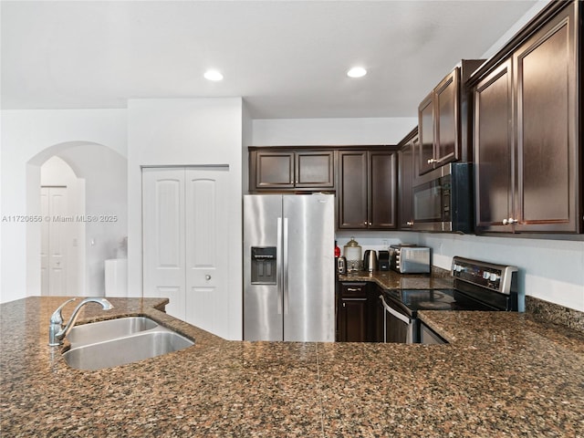 kitchen with dark brown cabinetry, stainless steel appliances, dark stone countertops, and sink