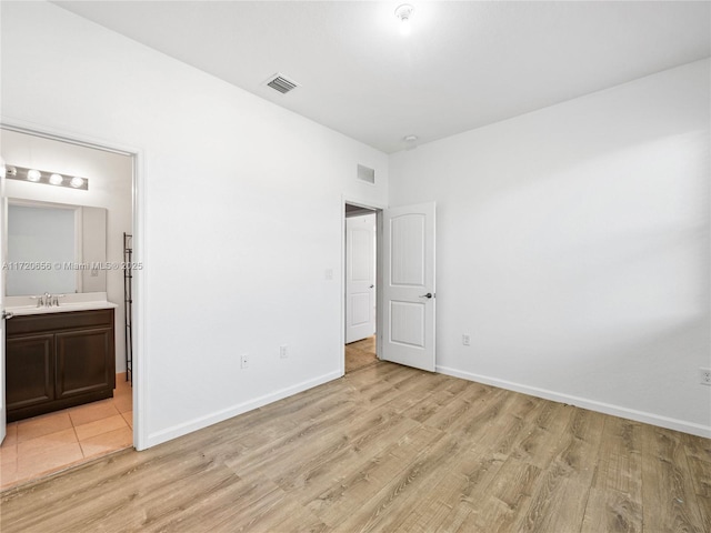 unfurnished bedroom with ensuite bathroom, light hardwood / wood-style flooring, and sink