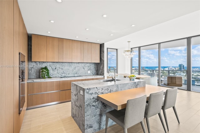 kitchen with a center island with sink, black electric stovetop, pendant lighting, decorative backsplash, and sink