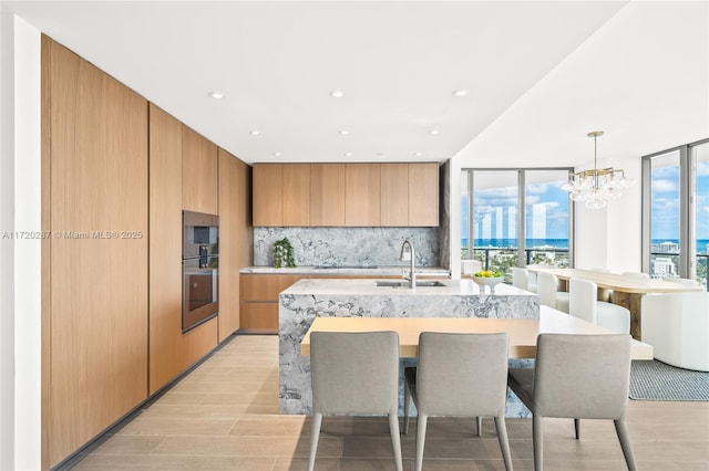 kitchen featuring tasteful backsplash, an island with sink, a wall of windows, and pendant lighting