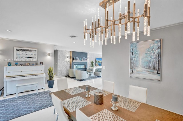 dining space featuring tile patterned flooring, crown molding, a large fireplace, and a notable chandelier