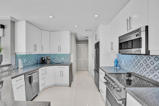 kitchen with stainless steel appliances, white cabinetry, tasteful backsplash, and dark stone counters