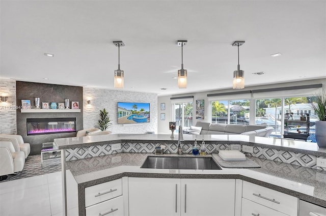 kitchen featuring white cabinetry, sink, decorative light fixtures, and a large fireplace